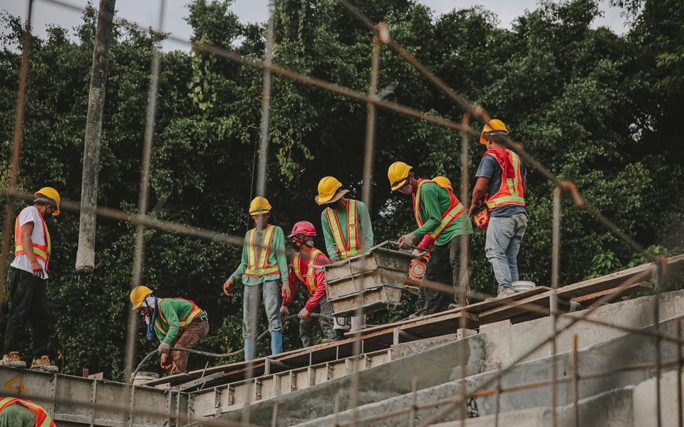 Group of about eight construction workers in hard hats and orange/green hi-vis v