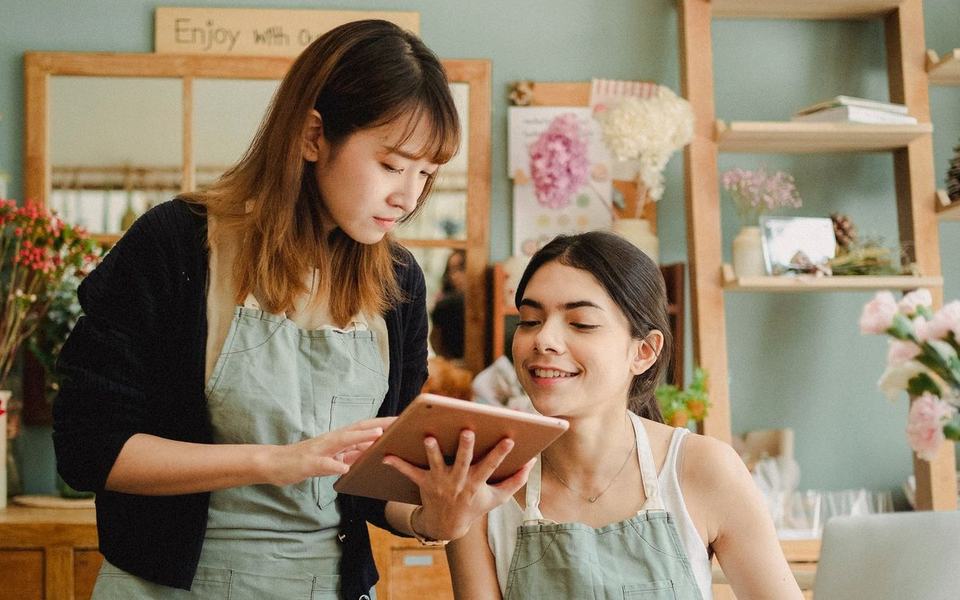 Florist-shop manager showing a tablet to a smiling younger colleague in a small