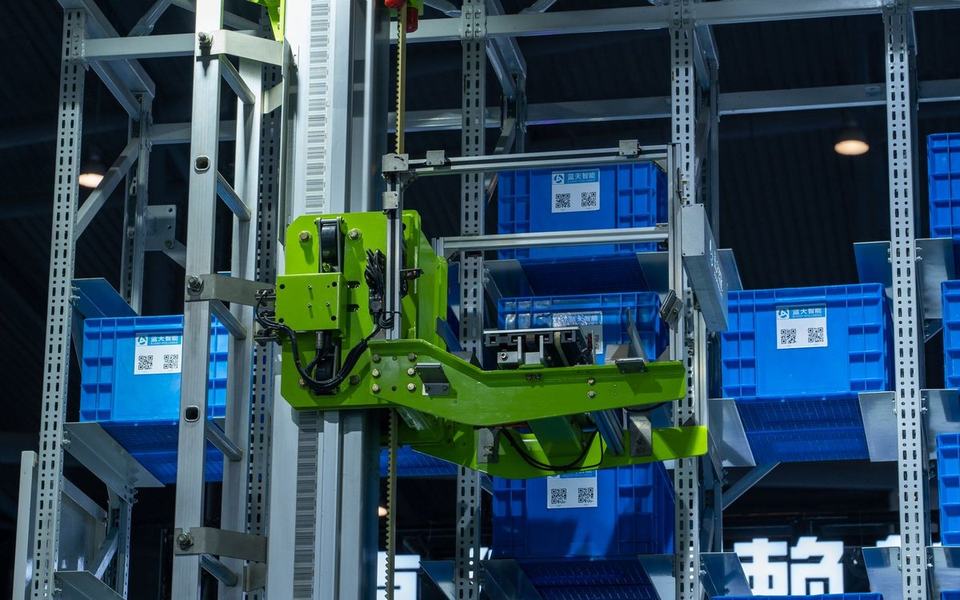 Green automated picker arm on a rack gantry handling blue storage crates in an a